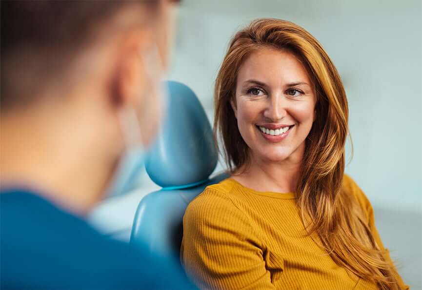 smiling woman sitting in a dental chair while talking with her dentist