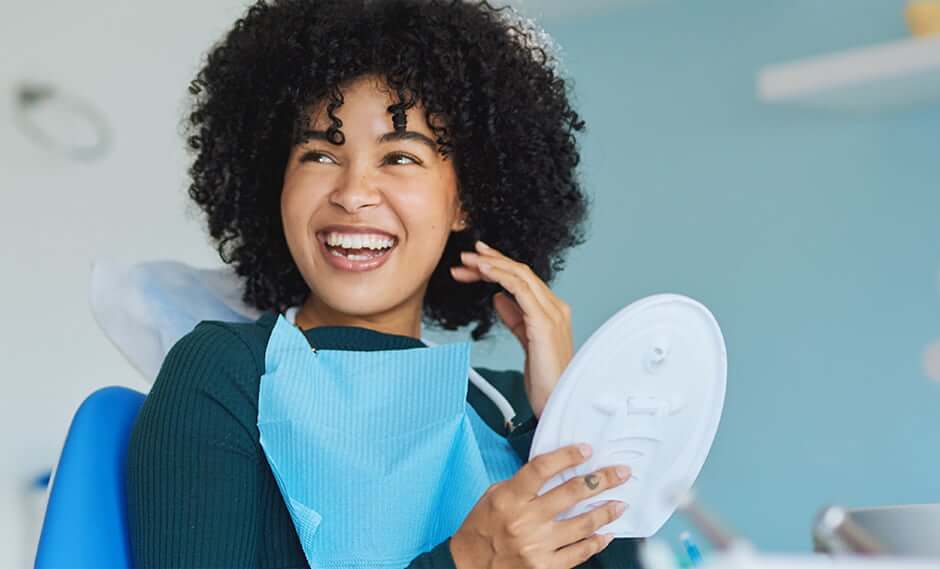 woman examining her smile in a mirror while sitting in a dental chair