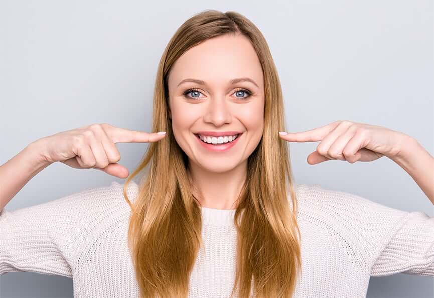 woman pointing to her bright, white smile