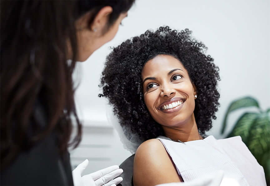 smiling woman sitting in a dental chair while talking with her dentist